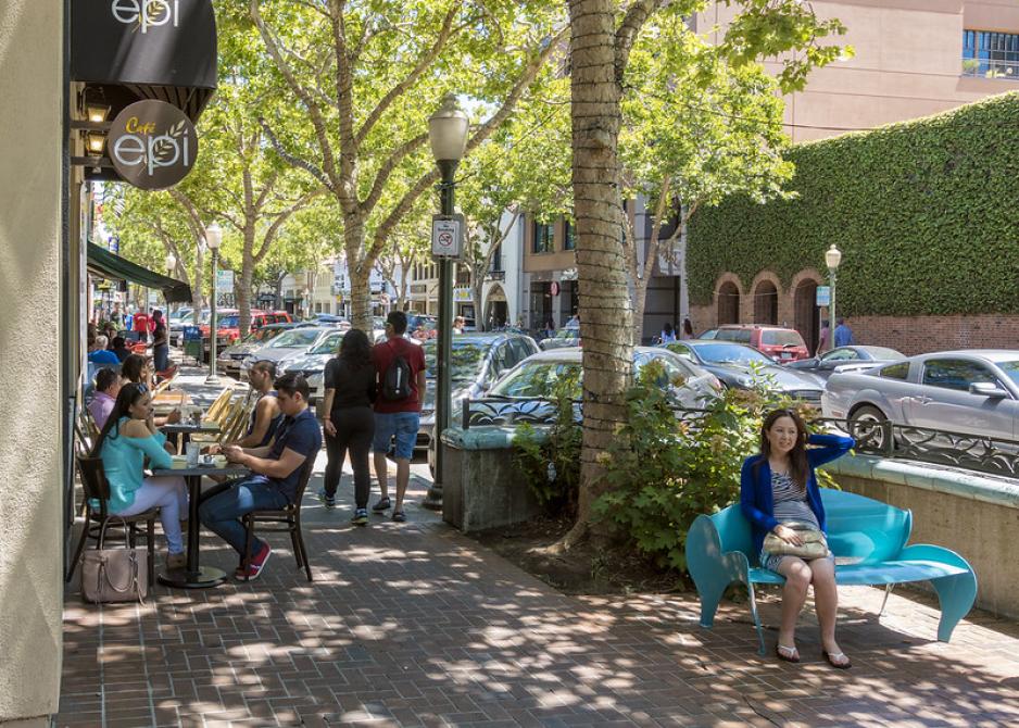 A photo of a main street sidewalk with people sitting at cafe and street seating.