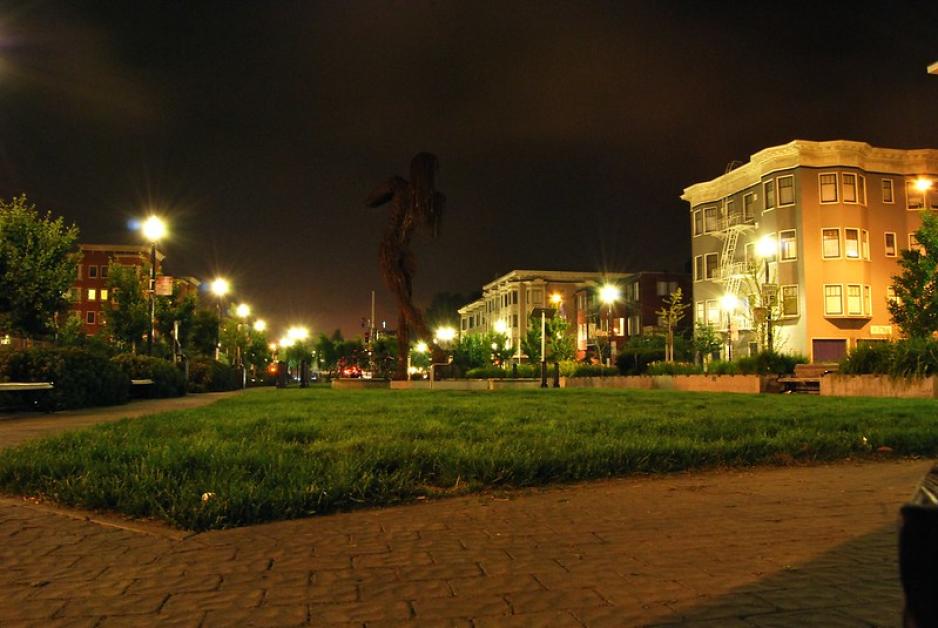 Photo of a common space covered in grass and walkways surrounded by taller buildings at night