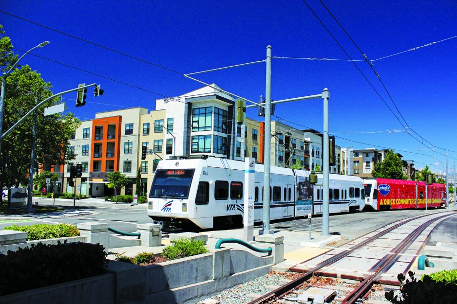 Photo of a pedestrian crossing across a VTA light rail tracks. VTA light rail train approaching.