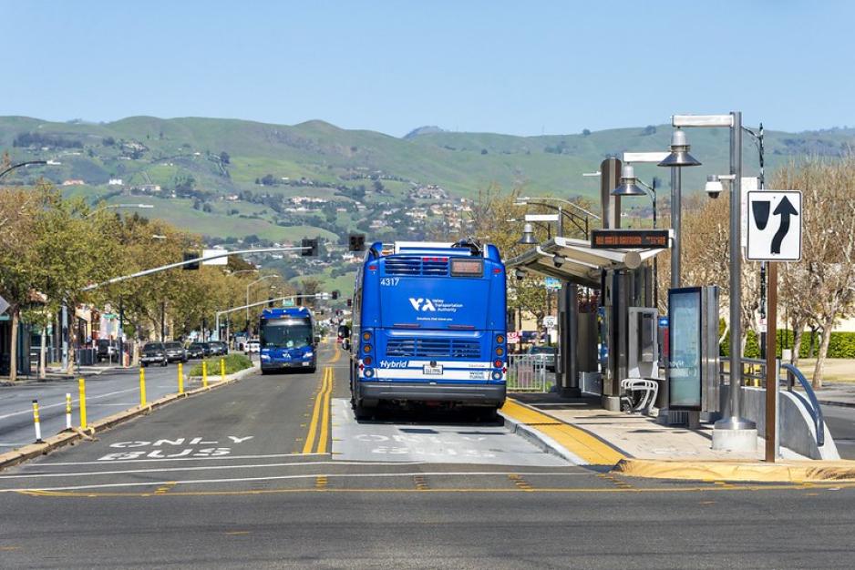 Photo of a center-running, two-way, bus-only lane with a concrete pad at the bus stop. VTA bus stopped at the bus stop.