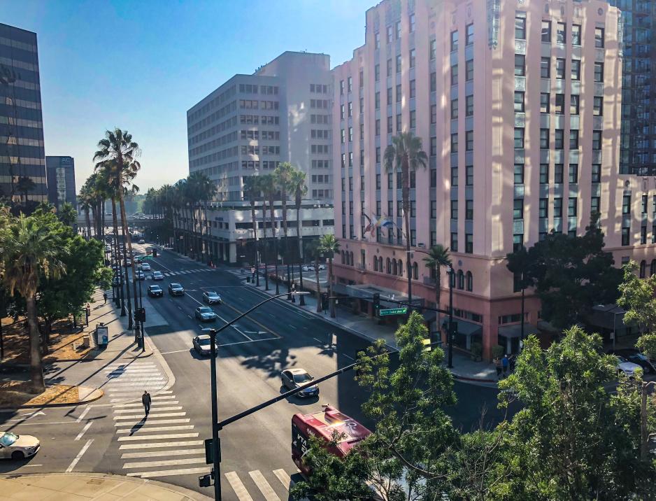 A photo of a street with high rise buildings and a street with crosswalks, wide sidewalks and trees.