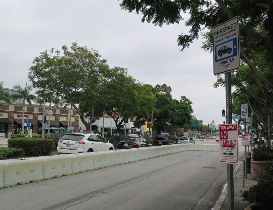 A photo of a street  with a blocked off lane for pick-ups/drop-offs.