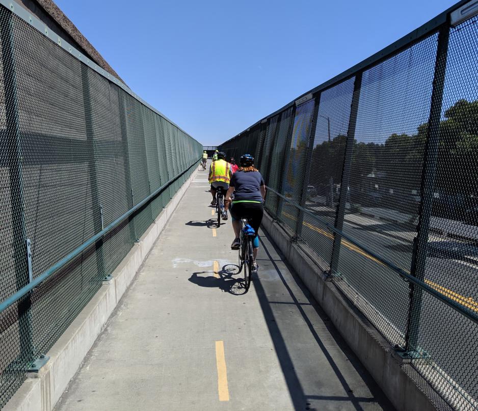 Photo of bicyclists riding up a bicycle and pedestrian bridge on a clear day