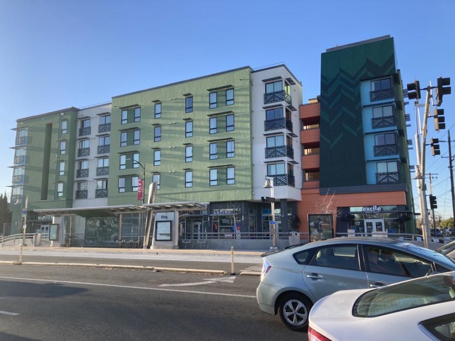 Photo of a colorful mixed-use building with a bus stop in front