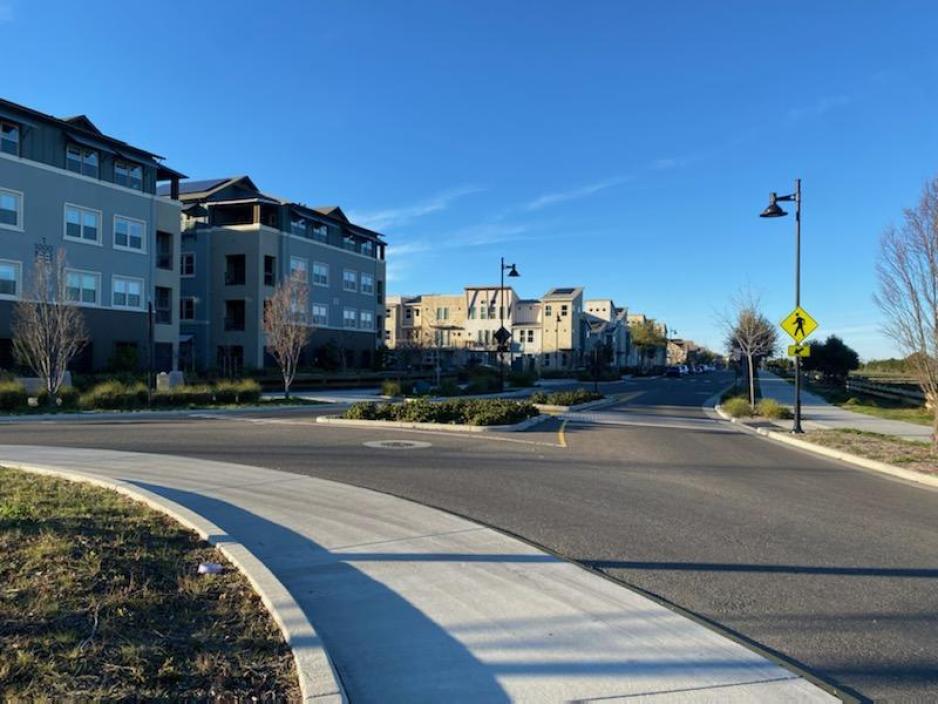 A photo of multiple four story apartment buildings and a street with a cross walk and median with plants.