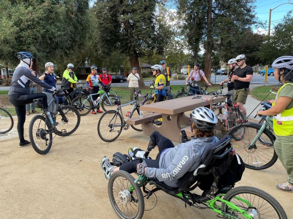 woman on recumbant bike near picnic table and group of other bicyclists