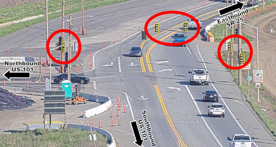 Aerial view of a roadway intersection under construction with temporary traffic signals in place. U.S. Highway 101 runs northbound and southbound through the center of the image, while State Route 25 crosses east–west. Temporary signal heads, highlighted with red circles, are installed on both sides of the intersection and in the center median to control traffic in all directions.