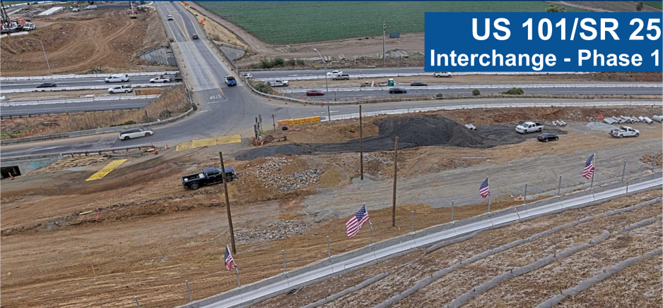 Aerial view of the US 101/SR 25 Interchange Phase 1 construction project showing the existing overpass, active highway traffic, construction areas with earthwork and equipment, surrounding farmland, and a project title banner in the upper right corner.