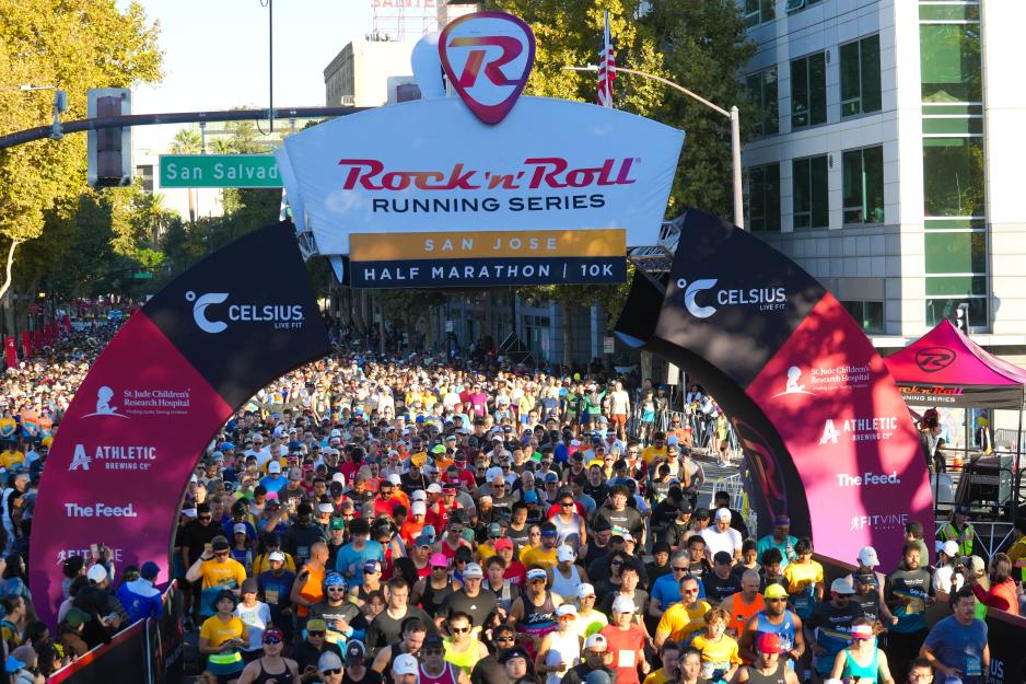 A large crowd of runners gathers beneath the Rock ‘n’ Roll San José Half Marathon and 10K starting arch in downtown San José.